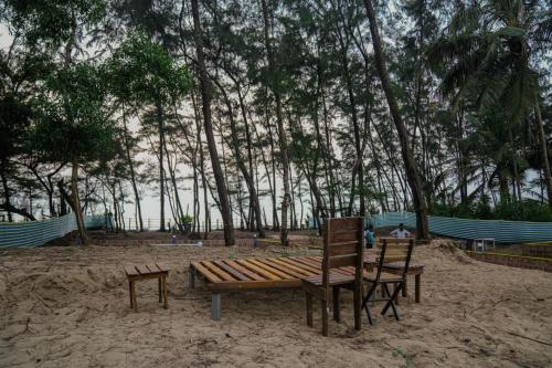 a wooden bench and two chairs on the beach at White Sand beach Stay Resort in Kumta