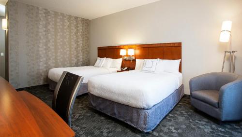 two beds in a hotel room with a table and a chair at Courtyard Rochester Brighton in Rochester