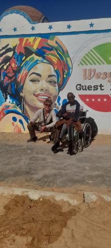 a group of three people sitting in a wheel chair in front of a mural at Wesy Ka Guest House in Aswan