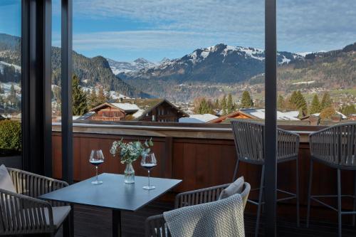 a table and chairs on a balcony with wine glasses at Miiro The Mansard in Gstaad