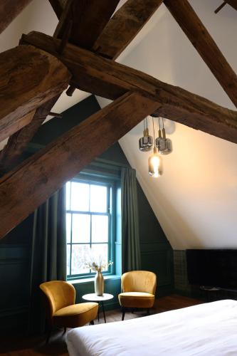 a bedroom with a bed and two chairs and a window at Stadshotel Geertruidenberg in Geertruidenberg