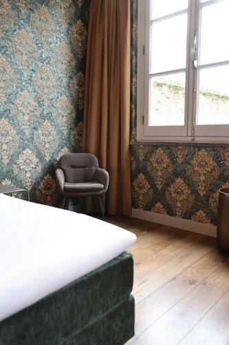 a bedroom with a bed and a chair and a window at Stadshotel Geertruidenberg in Geertruidenberg