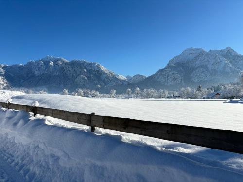 a fence covered in snow with mountains in the background at Jägerhof und Jägerstadel in Schwangau