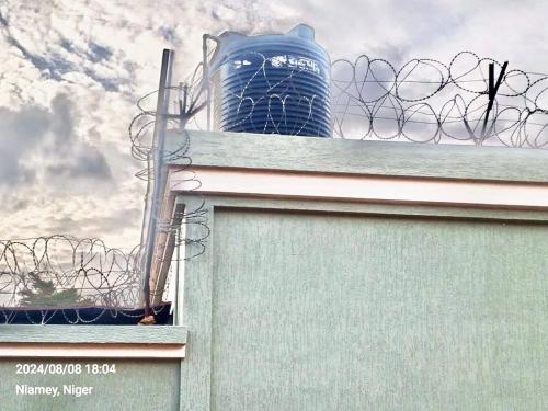 a fence with barbed wire and a tower in the background at La villa dolive in Niamey