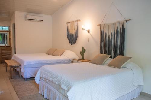 two beds in a room with white sheets at Refugio Surf Lodge in Tamarindo