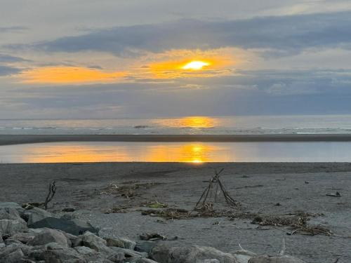 a sunset on a beach with the sun reflecting in the water at On the Beach in Hokitika