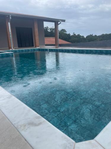 a swimming pool with blue water in front of a house at Chácara encantadora Ibiuna in Ibiúna
