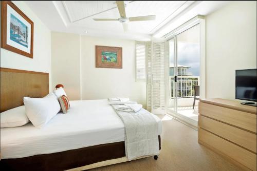 a white bedroom with a bed and a television at The Pool Resort Kingscliff - Private Apartments by Holiday Management Company in Kingscliff