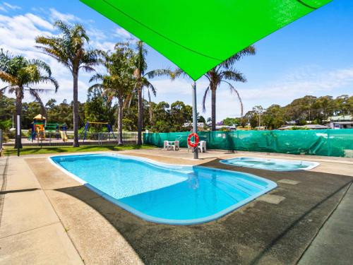 a swimming pool with an umbrella and a playground at Lakes Entrance Tourist Park in Lakes Entrance