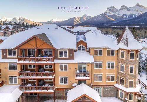 a building covered in snow with mountains in the background at Falcon Crest Lodge by CLIQUE in Canmore