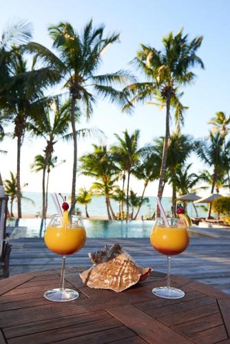 two glasses of orange juice on a wooden table near the ocean at Tiamo Resort in Kemps Bay