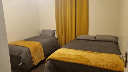 two beds in a room with yellow curtains at Apple valley in Manchester