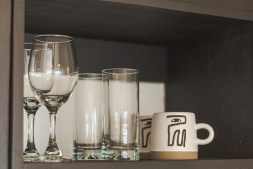three wine glasses and a mug on a shelf at Loft By Toore Patagonia in Puerto Natales