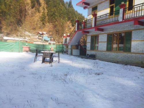 a table and chairs in the snow in front of a building at Orange sky home stay gadaGushaini near jibhi in Jibhi