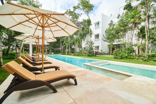 a row of chairs with umbrellas next to a swimming pool at Zama Condo with 2 Pools, Gym, Yoga Deck and BBQ Grill in Top Location in Tulum