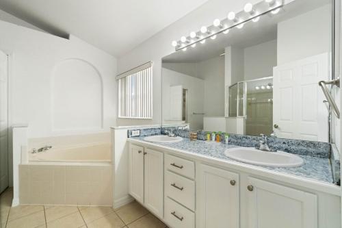 a bathroom with two sinks and a tub and a mirror at Luxury 4-Bedroom Home with Private Pool, Jacuzzi, AC, Wi-Fi, Cable TV, 5 Minutes from Disney in Kissimmee