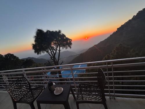 a table and chairs on a balcony with a sunset at Urban wave 2Bed rooms by Vanasthali in Kasauli