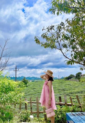a girl in a pink dress and hat standing in a field at SAKURA House - Vườn Đào in Mộc Châu