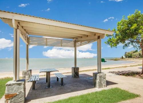 a picnic shelter with two benches in front of the beach at Modern Beach Apartment in Gladstone