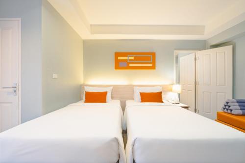 two beds in a room with white walls and orange pillows at Koon Hotel Sukhumvit in Bangna