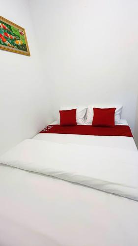 a white bed with two red pillows on it at Djuragan Kamar Halona in Ngemplak