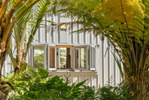 a white house with windows and plants at The Grass is Greener Getaway - Private Hot Tub in Whangamata