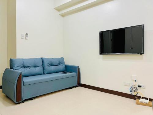 ein blaues Sofa in einem Zimmer mit einem Fernseher an der Wand in der Unterkunft Fairlane Residences in Manila