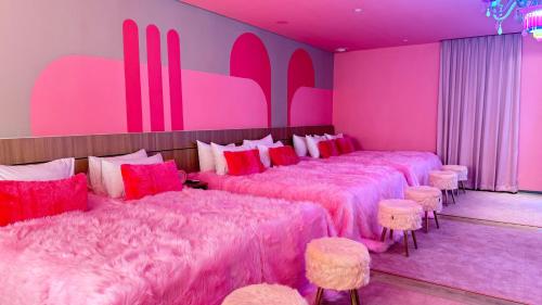 a room with four beds with pink covers and stools at Yellow Bee Resort Cililitan in Jakarta