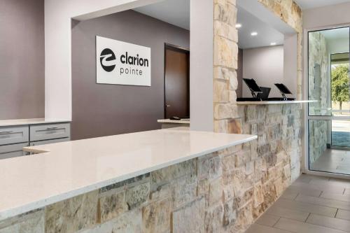 an office lobby with a white counter and a stone wall at Clarion Pointe - Fort Worth Arlington West in Fort Worth