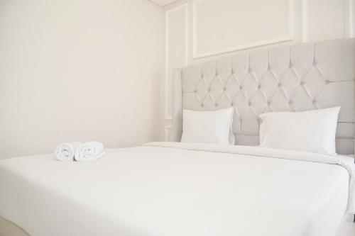 a white bed with two wedding rings on it at Modern Look and Warm 1BR at Gold Coast Apartment By Travelio in Jakarta