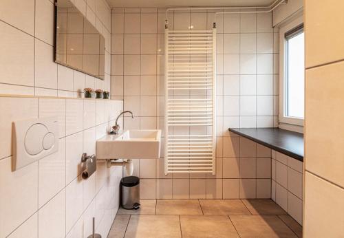 ein weiß gefliestes Bad mit einem Waschbecken und einem Fenster in der Unterkunft Bungalowpark Simpelveld - Schakel 6 in Simpelveld