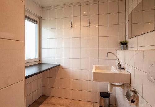 a white tiled bathroom with a sink and a window at Bungalowpark Simpelveld - Schakel 5 in Simpelveld