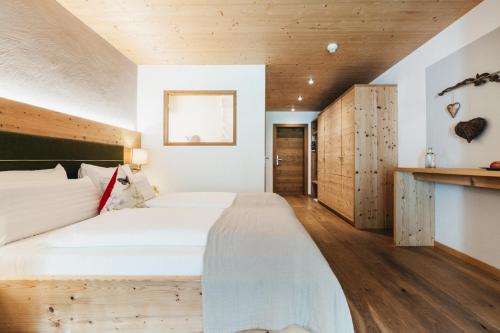 a bedroom with a large white bed and wooden floors at Biohotel Rupertus in Leogang