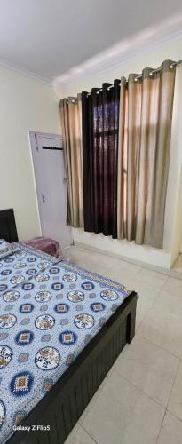 a bedroom with a bed with a blue comforter and curtains at Radha Krishna Sharnam in Chhatikara