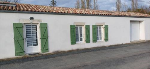 un bâtiment blanc avec des fenêtres à volets verts et une rue dans l'établissement Maison calme au bord de l'eau, à Marans