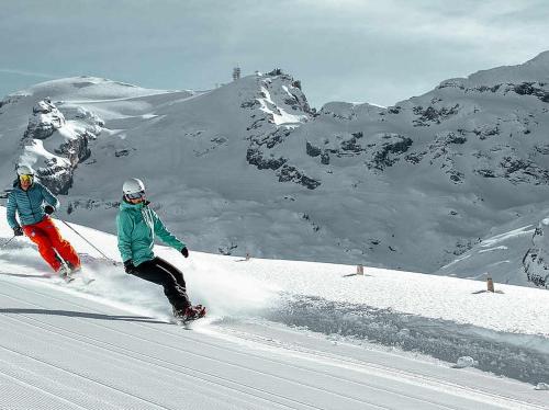 two people are skiing down a snow covered mountain at Hotel Alpina Einhorn - Self-Check-In in Wolfenschiessen