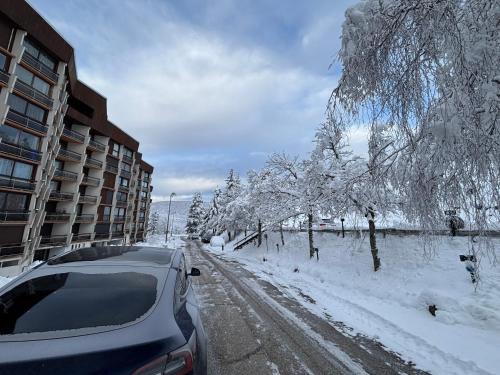 une voiture garée sur une route enneigée à côté d'un bâtiment dans l'établissement appartement Pied des Pistes à Villard de Lans Côte 2000 avec Ascenseur tout Equipée, à Prénatier