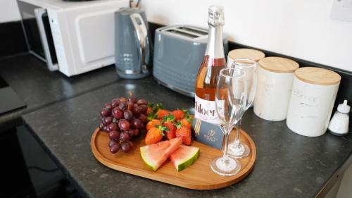 a wooden cutting board with fruit and a bottle of wine at Luxury 2 Guest House, Parking with EV , WIFI AND NETFLIX in Coventry