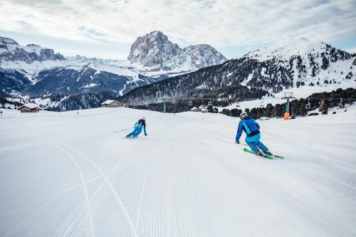 two people are skiing down a snow covered mountain at Adler Spa Resort Balance in Ortisei