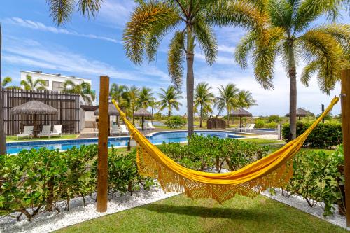 プライア・ド・フォルテにあるLuxo Térreo com Jardim IBERO Praia do Forteのヤシの木が茂るプールの前の黄色いハンモック