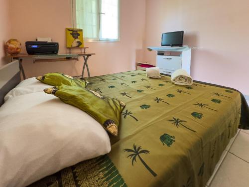 a bed with a green blanket with palm trees on it at Le Cocon Tropical - A 15min à pied de la plage in Sainte-Anne
