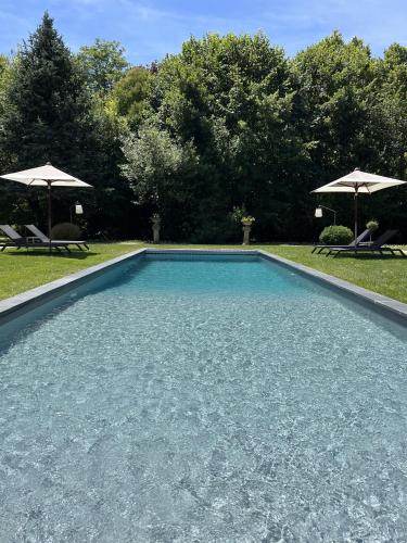 a swimming pool in a yard with two umbrellas at Clos Marcamps - Teritoria in Prignac-et-Marcamps
