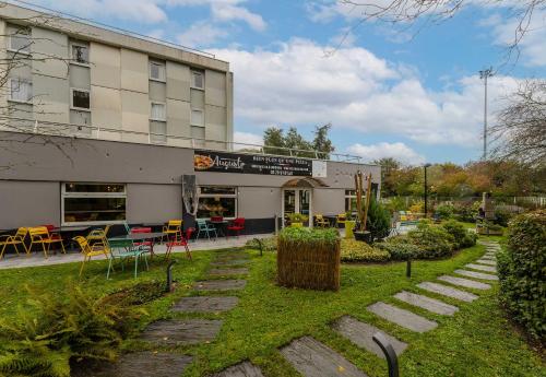 un bâtiment avec des tables et des chaises devant lui dans l'établissement B&B HOTEL Lille Villeneuve d'Ascq Grand Stade, à Villeneuve d'Ascq