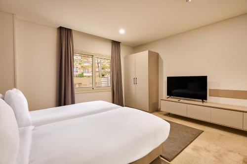 a white bedroom with a large bed and a flat screen tv at Brassbell l New Cairo l next to AUC in Cairo