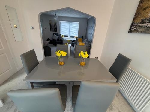 a dining room table with chairs and vases with yellow flowers at No 10, Ayr, 130m2, New Decor December 2024, All new entire 3 bedroom garden house in Ayr