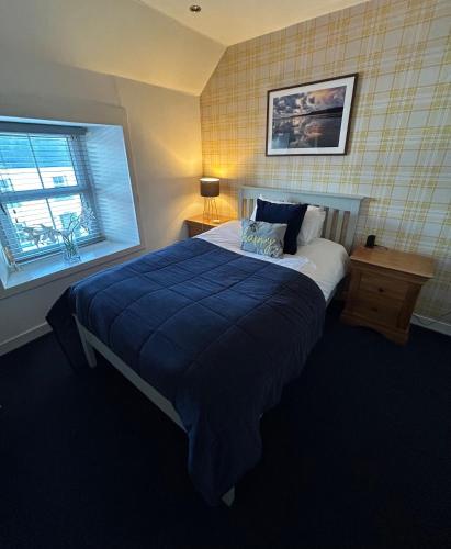 a bedroom with a bed with a blue blanket and a window at Lochindaal Hotel in Port Charlotte