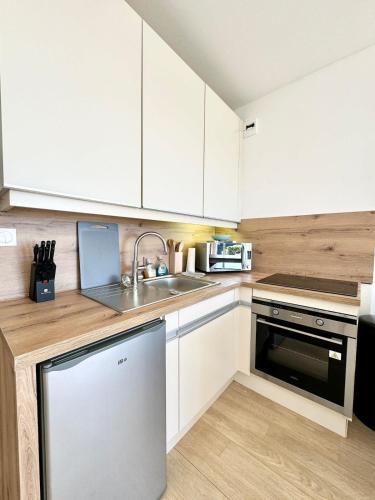 une cuisine avec des armoires blanches, un évier et un lave-vaisselle dans l'établissement Studio Cosy neuf Vue Mer Jardin et Terrasse, à Guidel