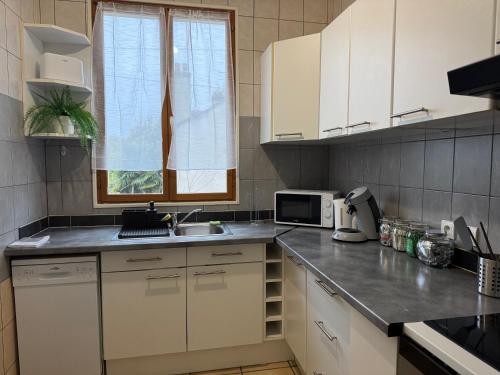 une cuisine avec des armoires blanches, un évier et une fenêtre dans l'établissement Le Nid Urbain, à Villemomble
