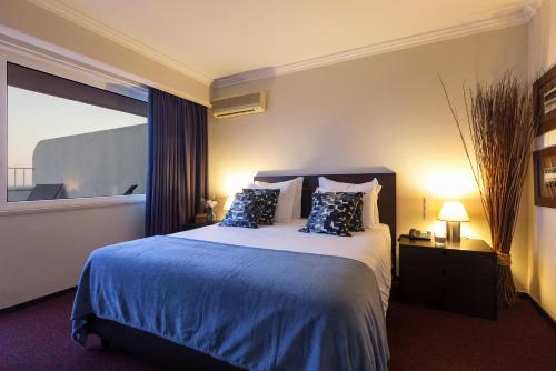 a bedroom with a bed with blue sheets and a window at Carcavelos Beach Hotel in Carcavelos