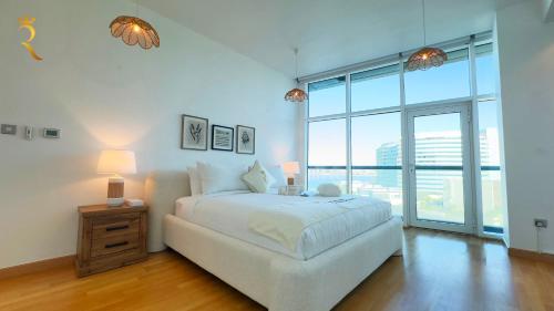 a white bedroom with a bed and a large window at Oceanview 2BR Bliss in Al Raha - Pool & Balcony Near Al Raha Beach in Abu Dhabi